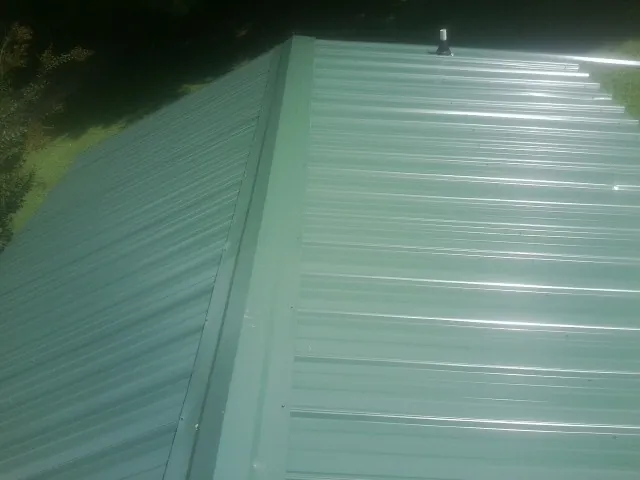 New green metal panels meeting at the ridge of a roof — Flat Roof Repair work by our crew in Barre