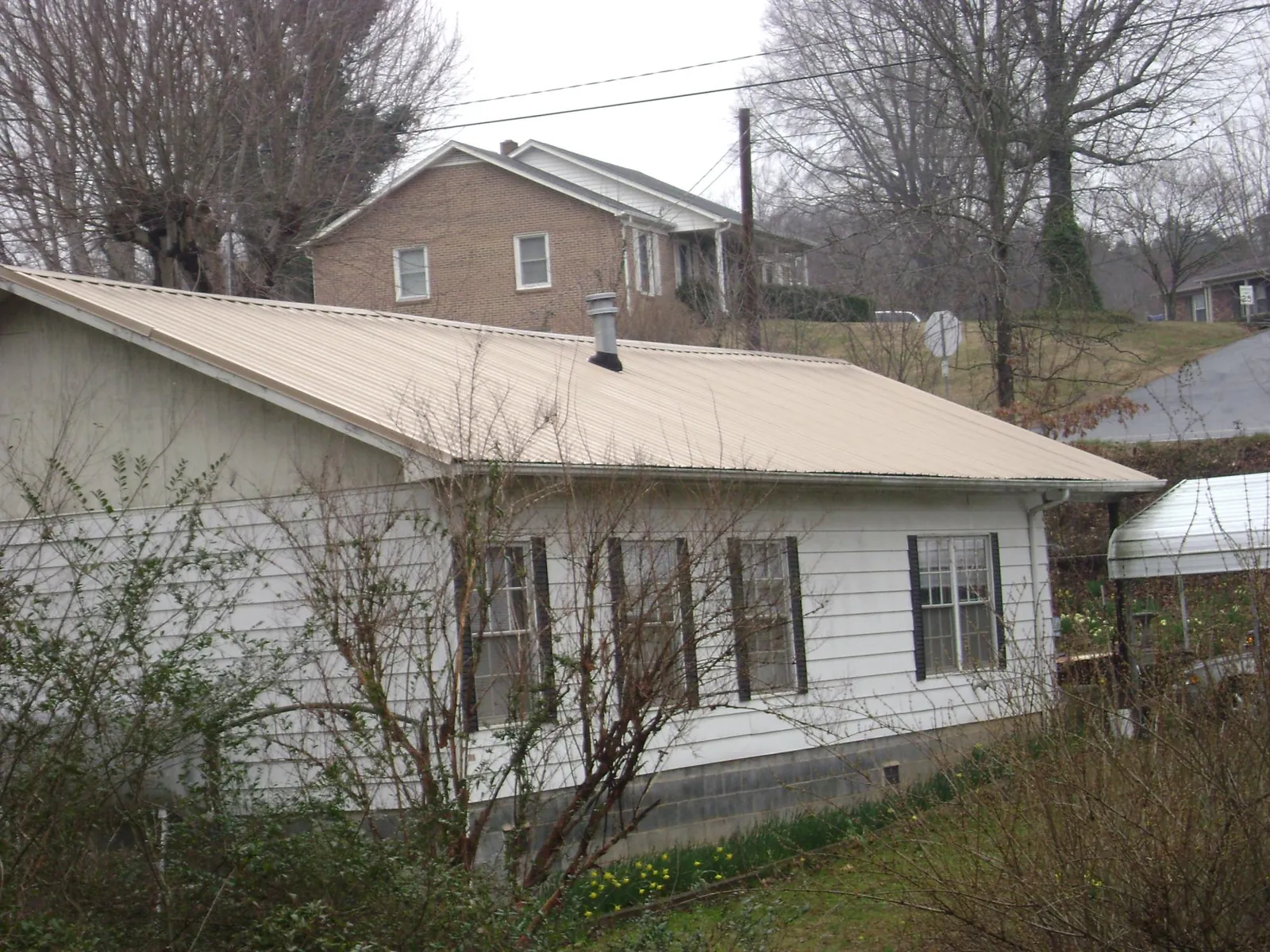 Tan metal roof on a white sided house set into a hillside — Commercial Roofing by Roofing Brothers in Barre