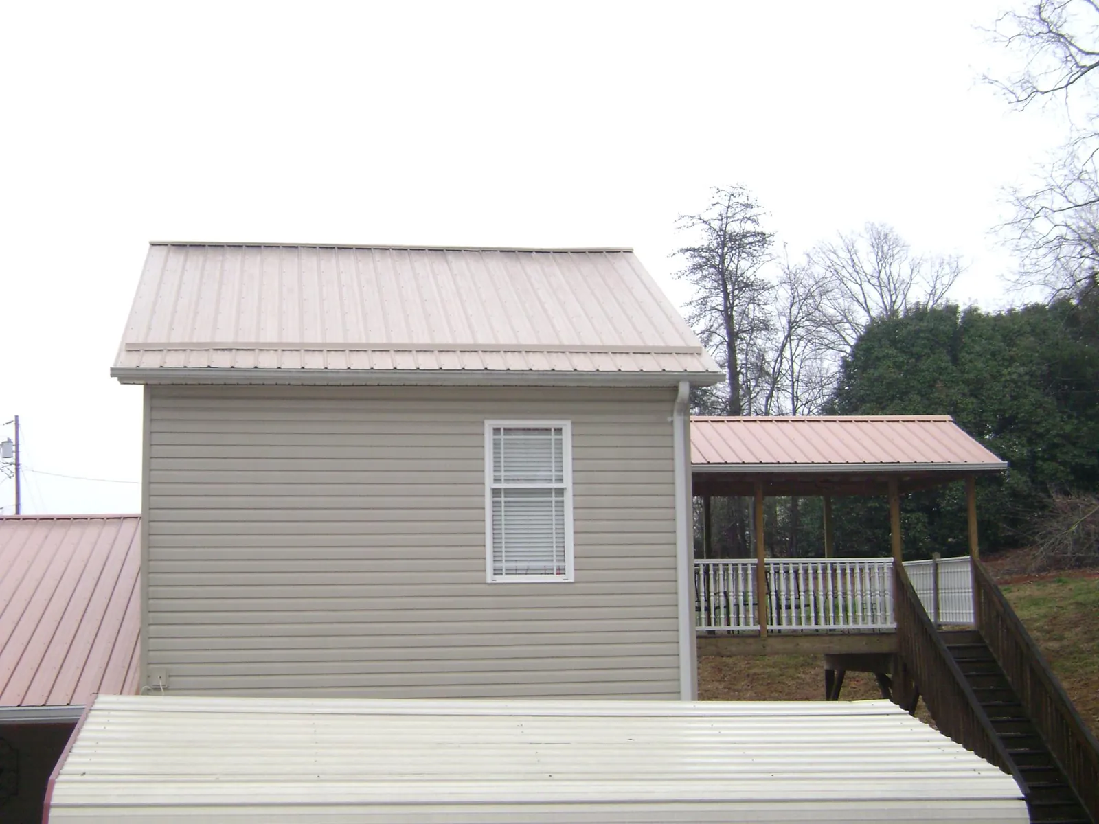 Tan metal roofs on a two story addition and attached porch, from a Roof Replacement job in Barre
